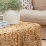 Woven ottoman with a plant and pillows on a beige sofa