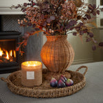 Decorative arrangement with a wicker vase, candle, and figs on a tray in a cozy room.