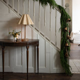 Decorative green garland on a staircase wall with a table and lamp in the foreground.