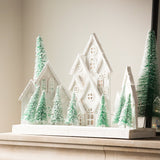 Charles Ted White Christmas Village Scene with snowy white houses and frosted green trees displayed on a mantel