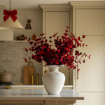 Kitchen with a white vase of red flowers on a counter, wooden stools, and a red bow decoration.