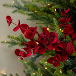 Decorative red flowers on a Christmas tree with lights in the background