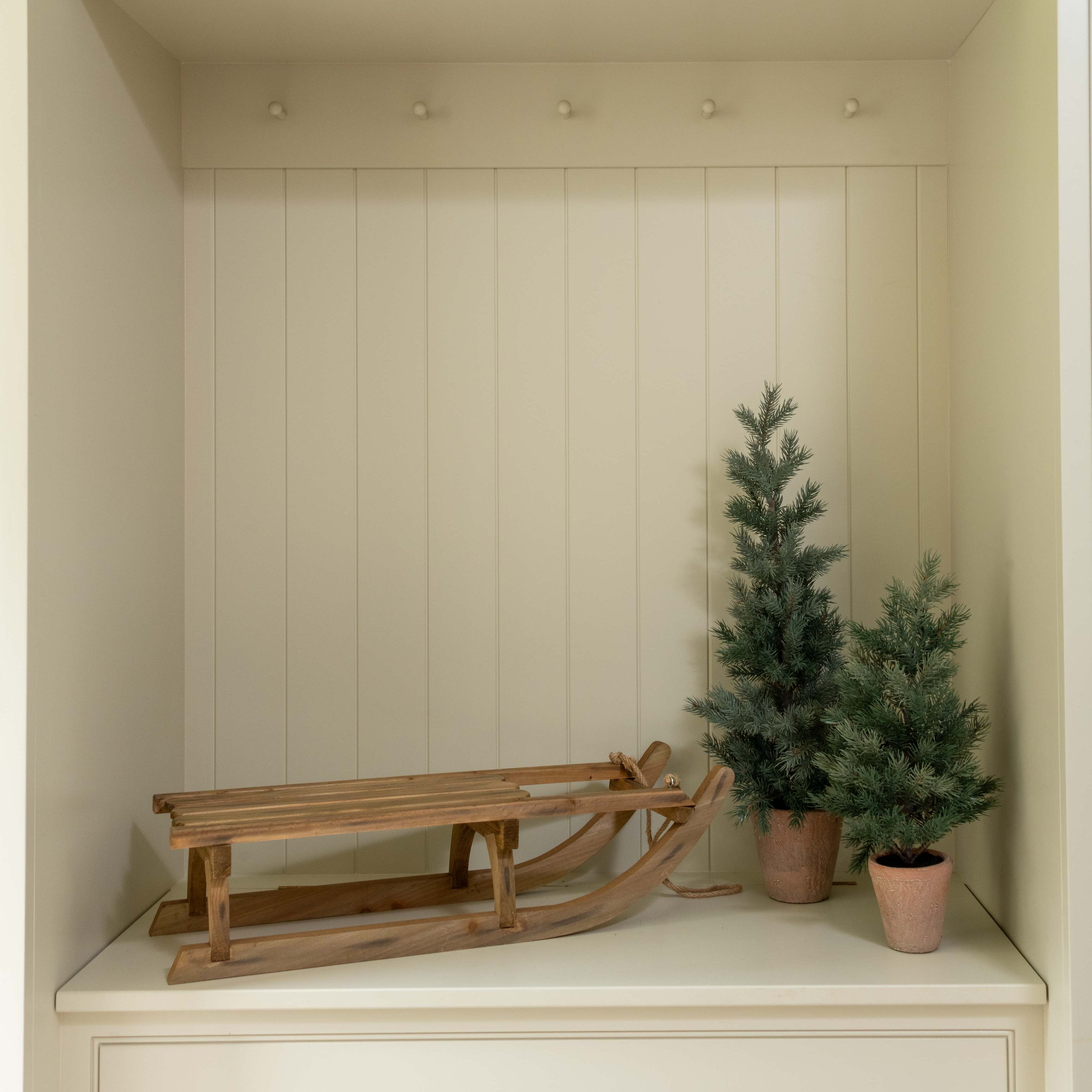 Small indoor space with white cabinets, a wooden sled, and two small potted trees.
