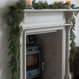White fireplace with green garland and candles on a white wall