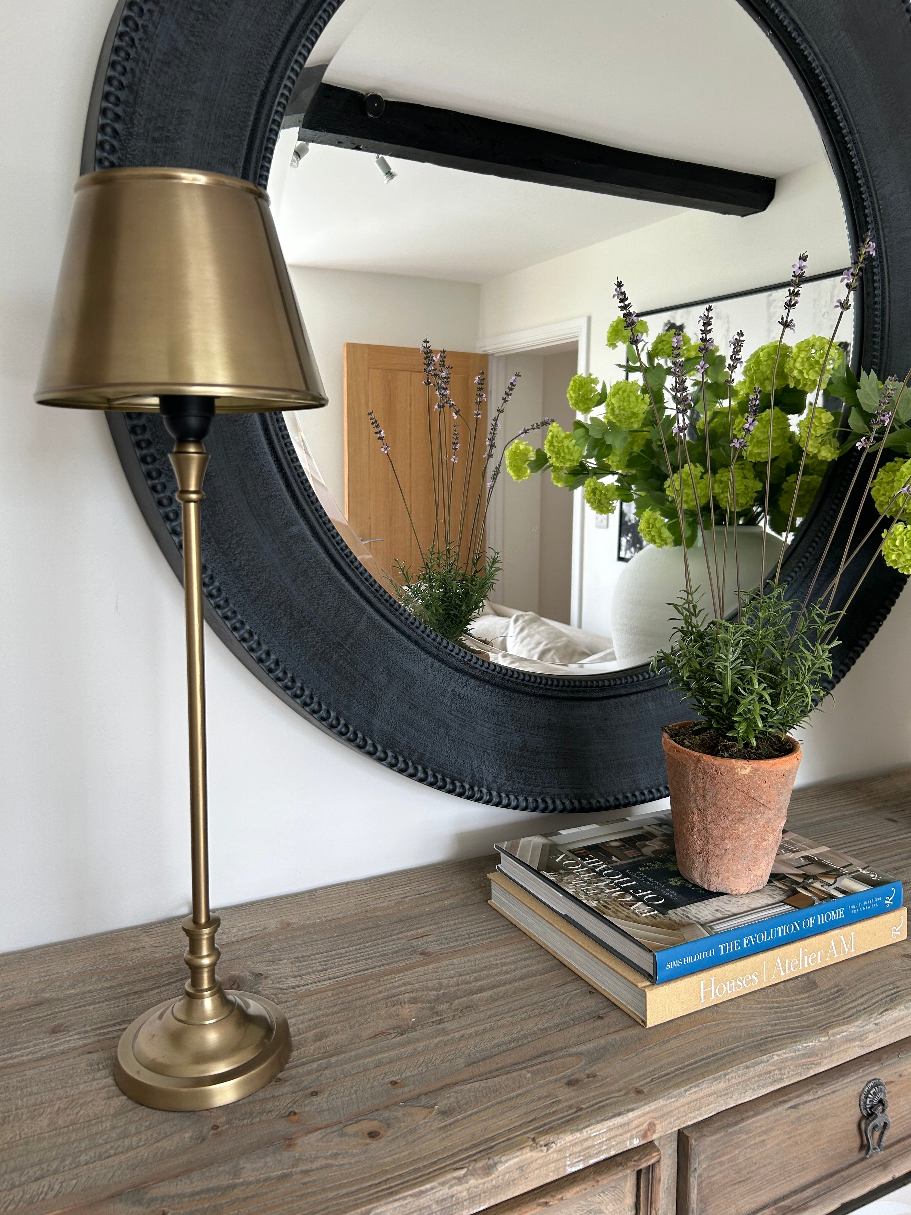 Brass table lamp styled on wooden console with round mirror and decor