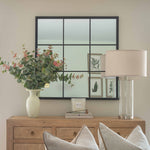 Decorative setup with a vase of flowers, mirror, lamp, and pillows on a wooden console table.