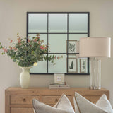 Decorative setup with a vase of flowers, mirror, lamp, and pillows on a wooden console table.