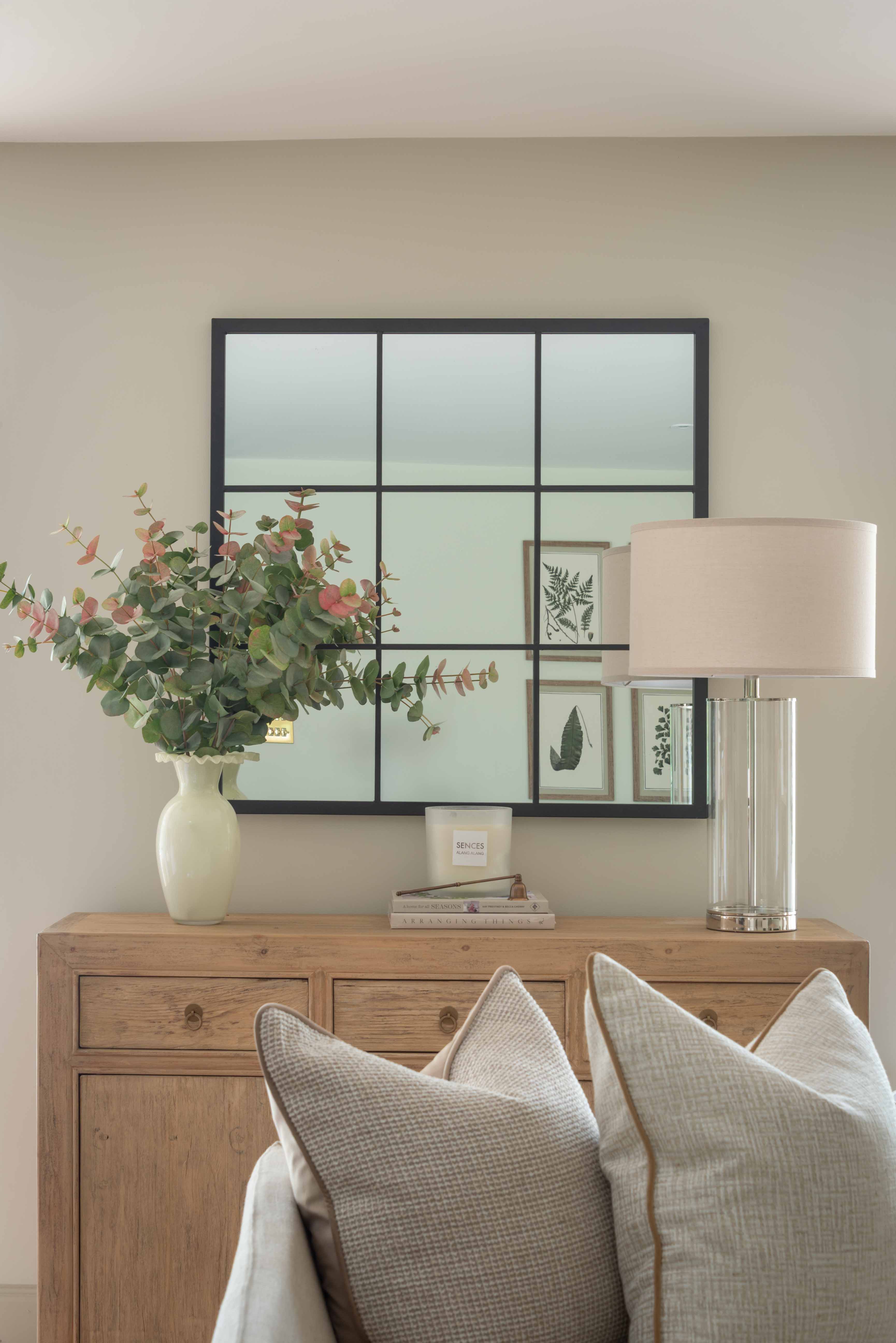 Decorative setup with a vase of flowers, mirror, lamp, and pillows on a wooden console table.