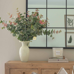 Decorative setup with a vase of flowers, books, and a candle on a wooden cabinet.