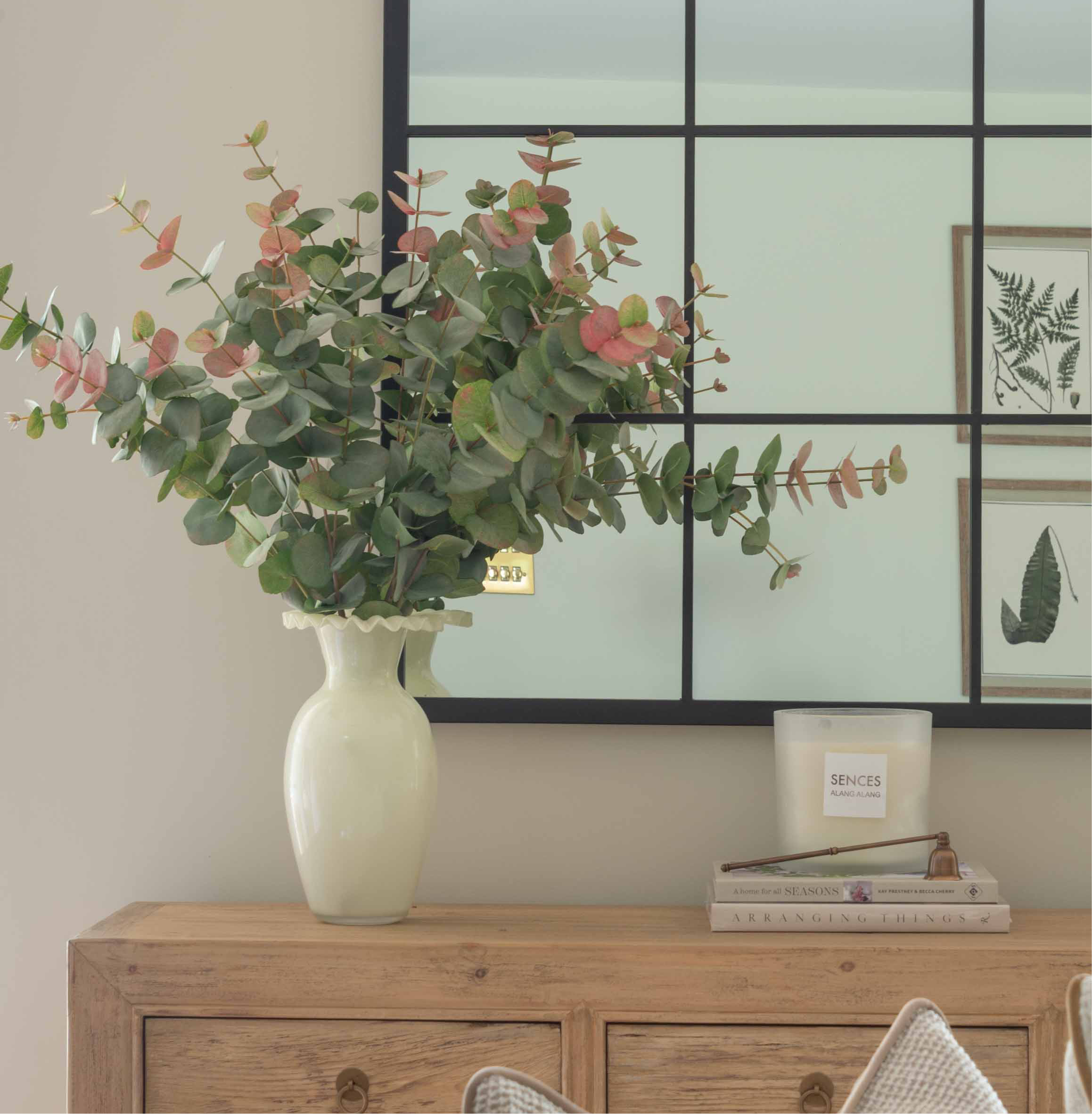 Decorative setup with a vase of flowers, books, and a candle on a wooden cabinet.