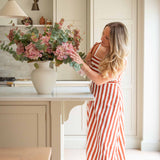 Woman in a red and white striped dress arranging flowers in a kitchen.