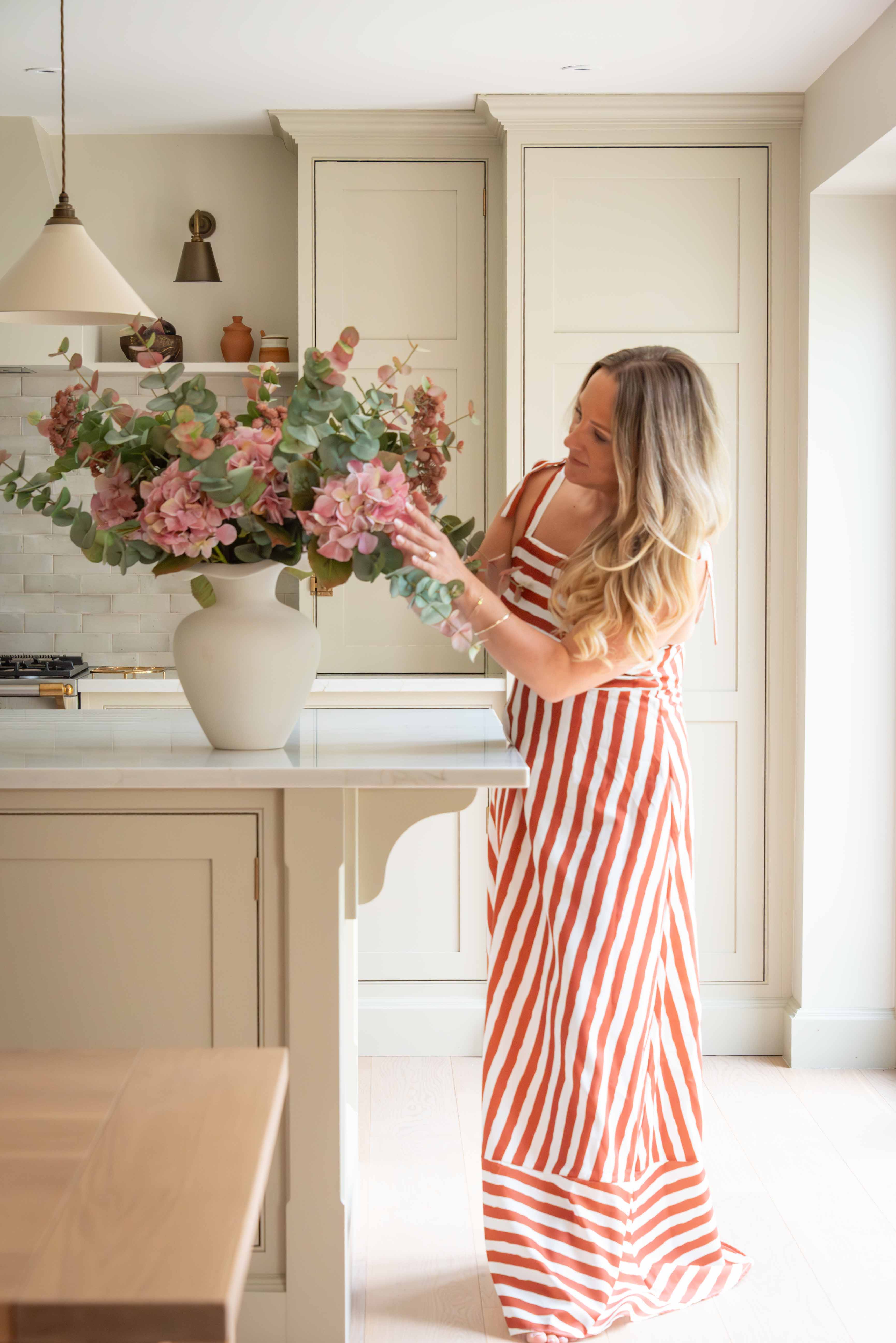 Woman in a red and white striped dress arranging flowers in a kitchen.