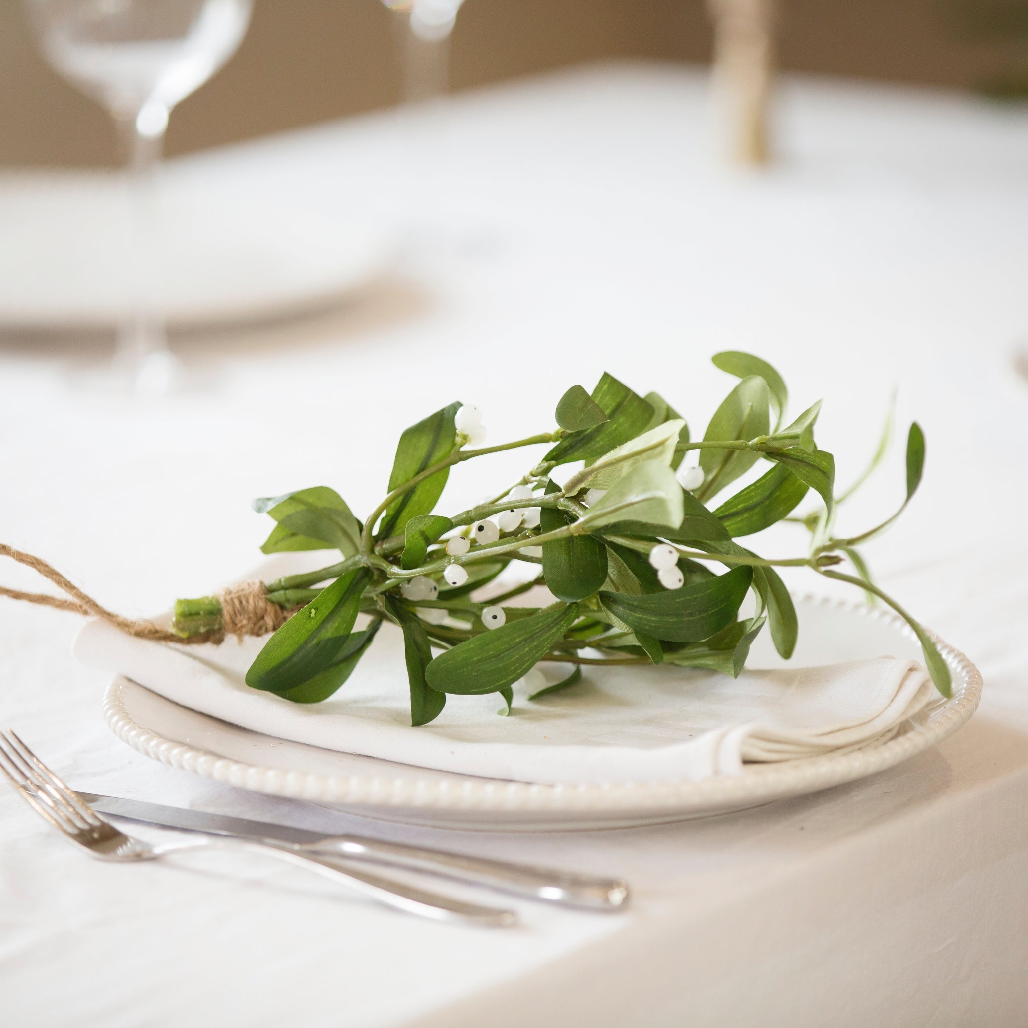 Faux Charles Ted Mistletoe Bundle with green leaves and white berries styled on a white plate at a festive table setting