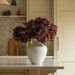Kitchen with beige cabinets, a vase of flowers on a counter, and wooden stools.