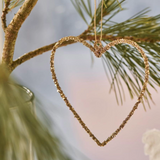 Gold heart-shaped ornament hanging on a branch with a blurred natural background