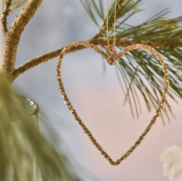 Gold heart-shaped ornament hanging on a branch with a blurred natural background