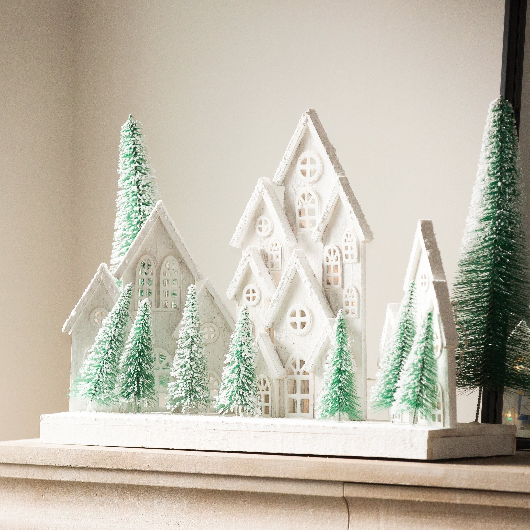 Charles Ted White Christmas Village Scene with snowy white houses and frosted green trees displayed on a mantel