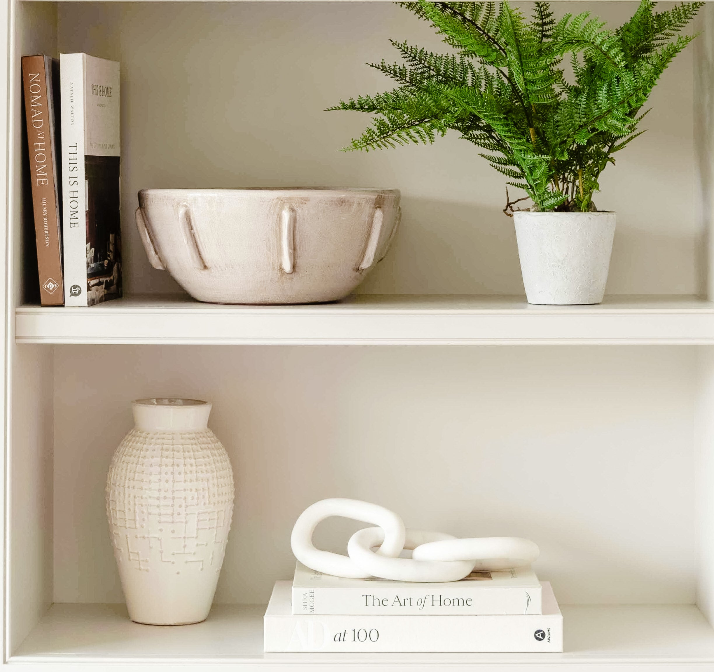 A stunning white ceramic vase sitting on a bookshelf. There is a raised-bump pattern on the exterior of the vase