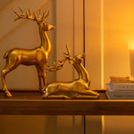 Gold deer figurines on a table with a candle and mirror in a warm-lit room.