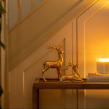 Gold deer figurines on a table with a candle and mirror in a warm-lit room.