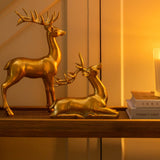 Gold deer figurines on a table with a candle and mirror in a warm-lit room.