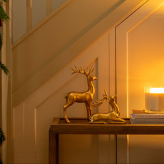 Gold deer figurines on a table with a candle and mirror in a warm-lit room.