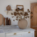 A large round beige vase filled with autumn florals