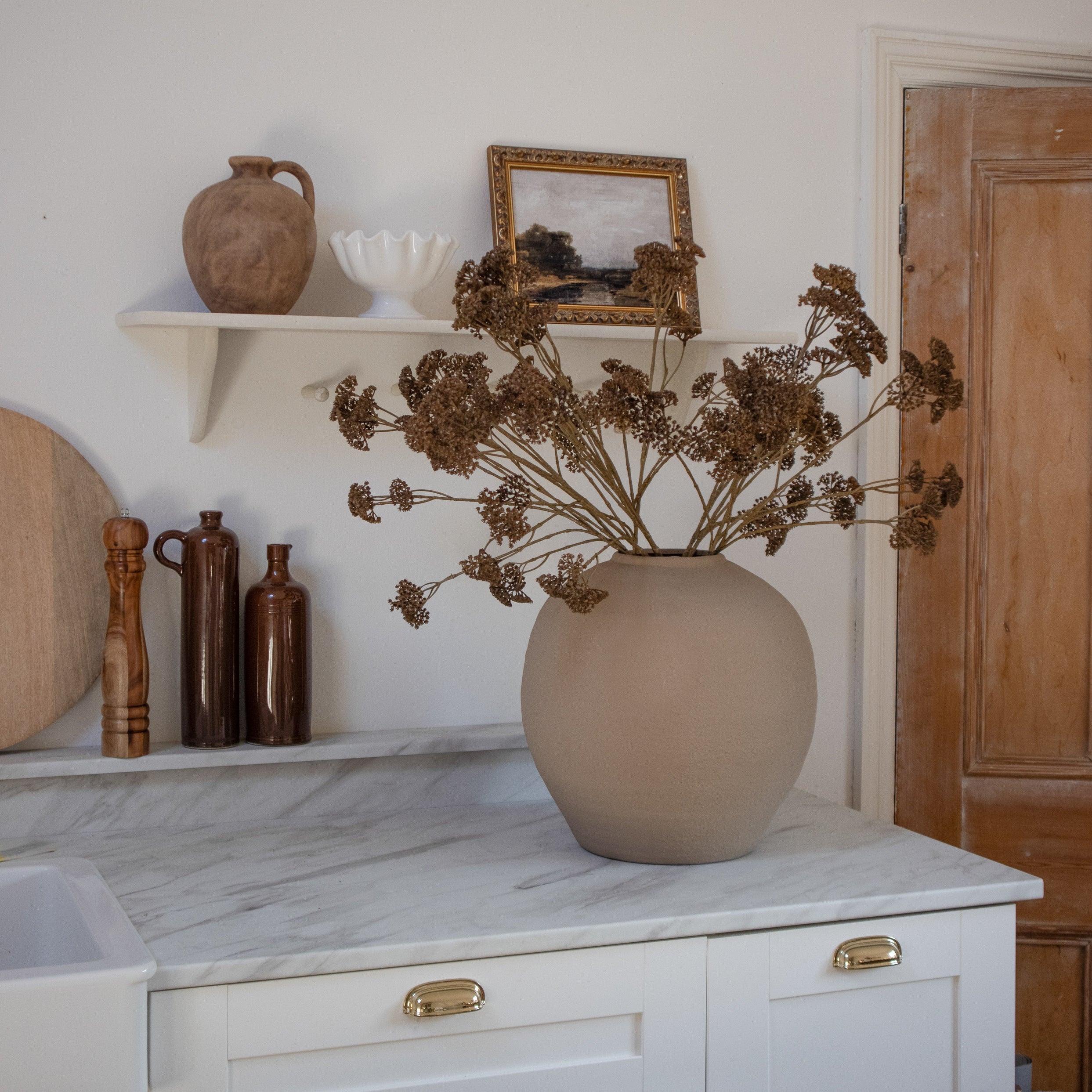 A large round beige vase filled with autumn florals