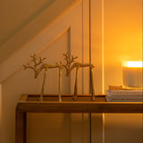 Decorative setup with gold reindeer sculptures and a candle on a table against a warm-toned wall.