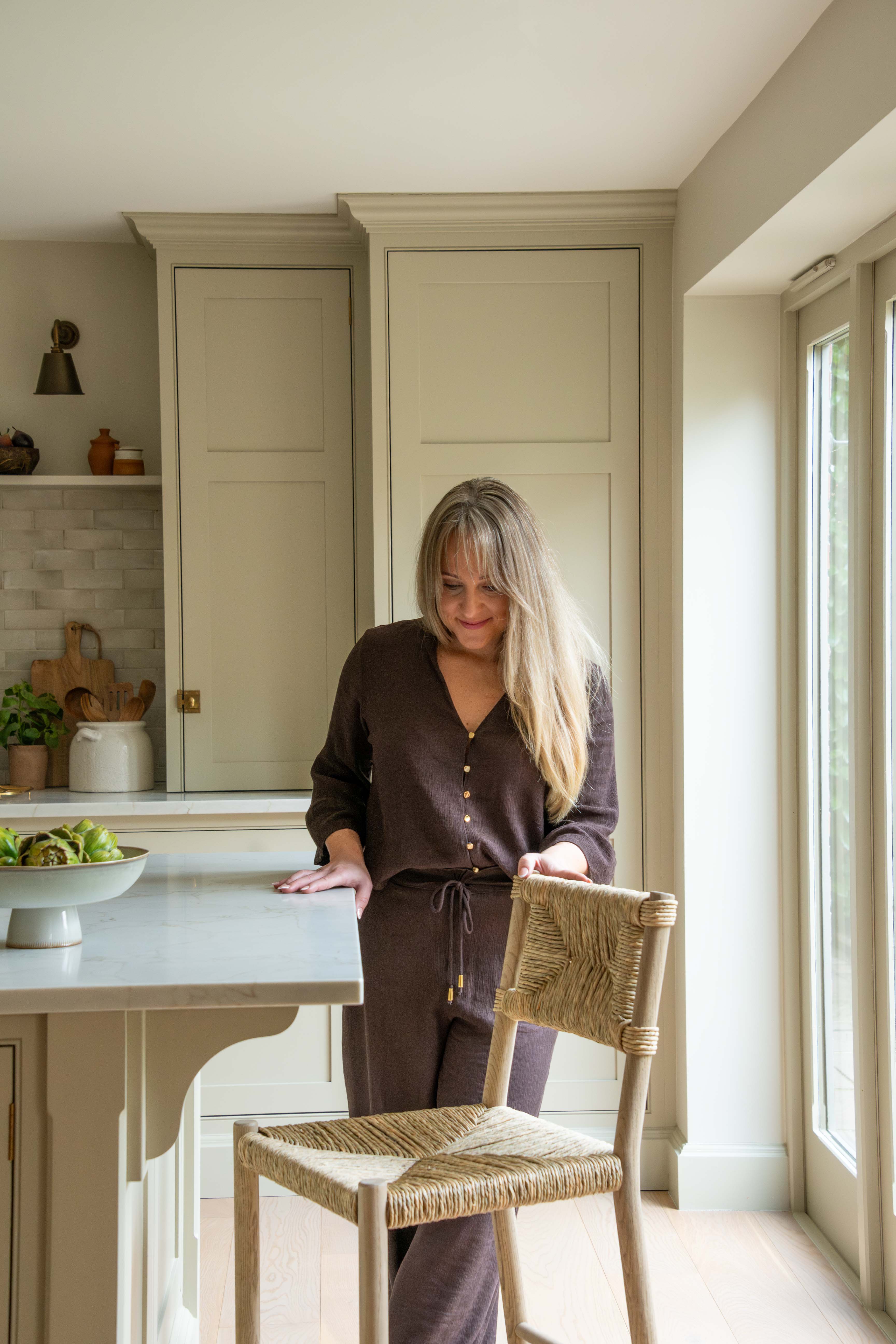 Woman standing in a kitchen next to a table with a bowl of fruit