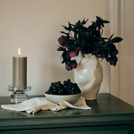 Decorative setup with a vase of flowers, bowl of grapes, and candle on a surface.