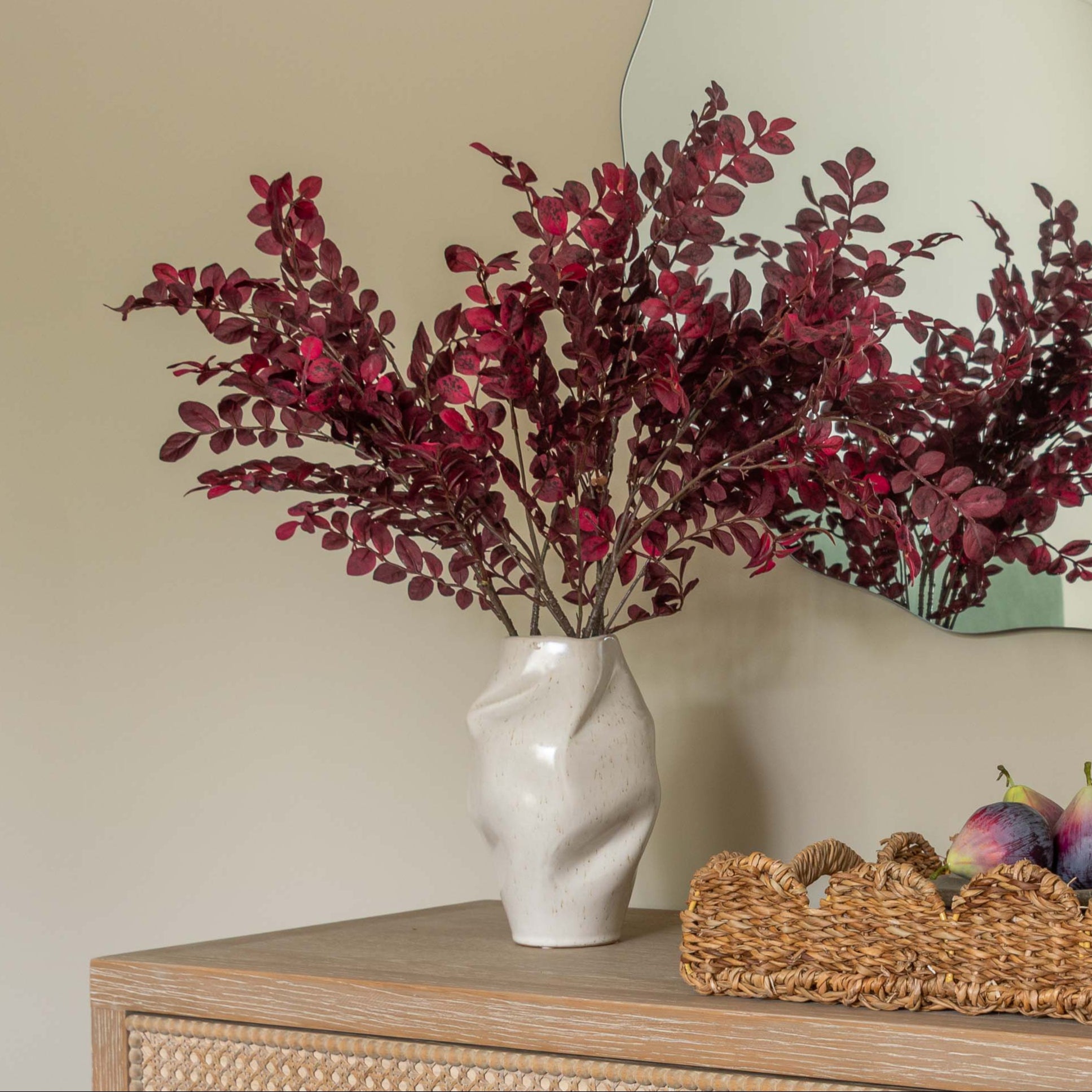 Beige dresser with wicker drawers, decorative flowers, and a mirror on a beige wall.