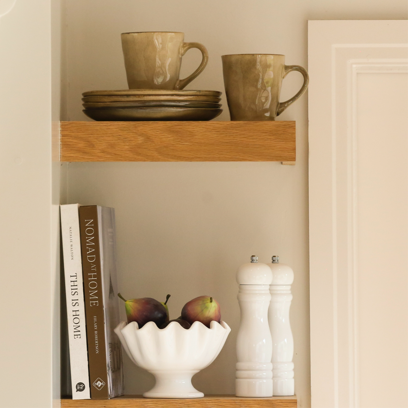 stoneware side plates stacked on a wooden shelf alongside mugs and home décor accessories