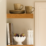 stoneware side plates stacked on a wooden shelf alongside mugs and home décor accessories