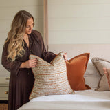 Woman arranging pillows on a bed in a bedroom setting
