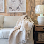 Cosy living room with beige sofa, blanket, and lamp against a wooden wall.