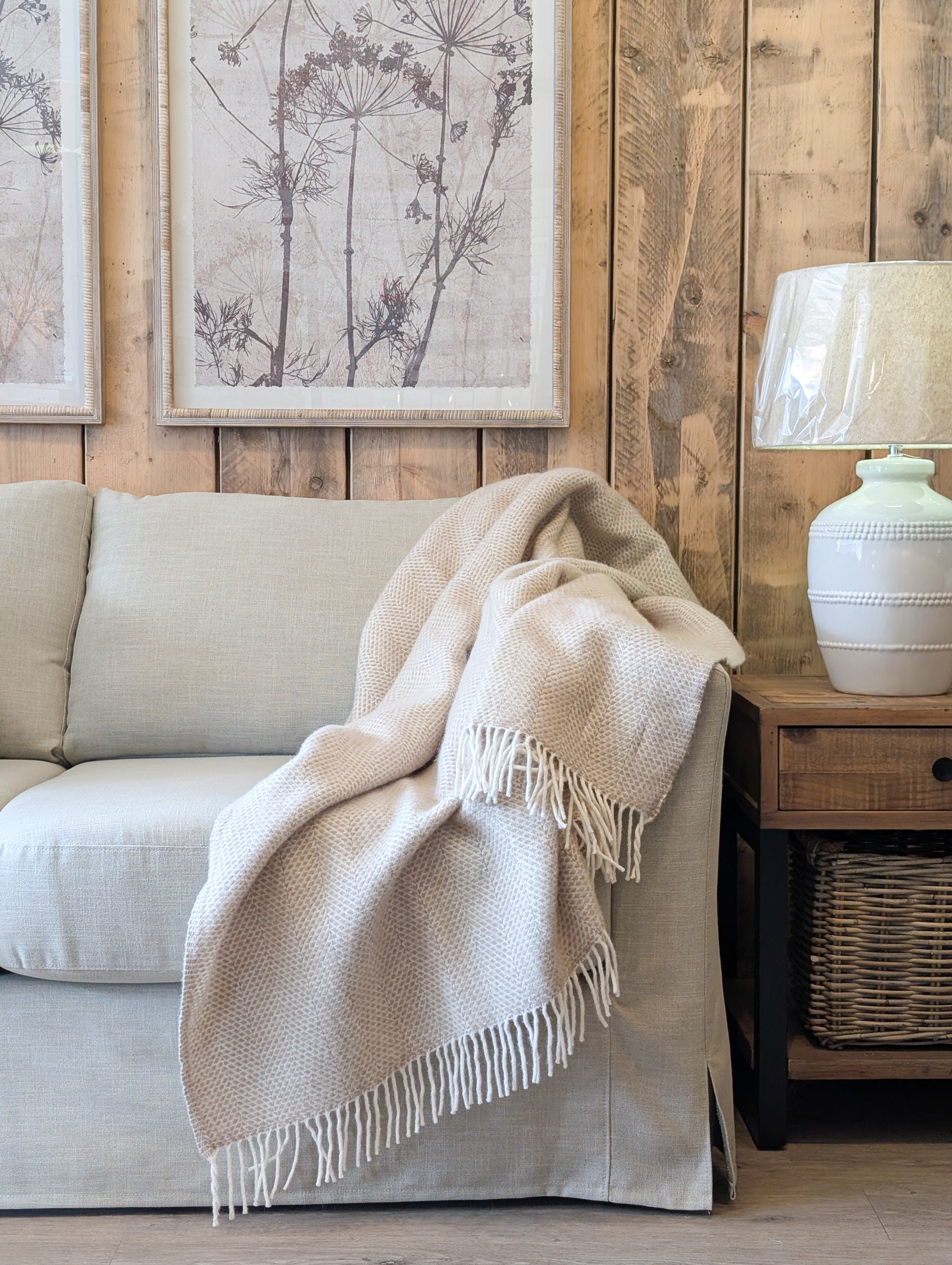 Cosy living room with beige sofa, blanket, and lamp against a wooden wall.