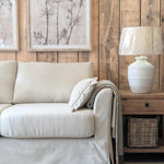 Beige sofa in a living room with wooden wall paneling and a lamp.
