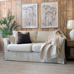 Beige sofa with decorative pillows and a blanket in a room with wooden walls and a lamp.
