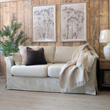Beige sofa with decorative pillows and a blanket in a room with wooden walls and a lamp.