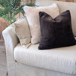 Beige sofa with decorative pillows against a wooden wall