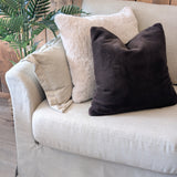 Beige sofa with decorative pillows against a wooden wall
