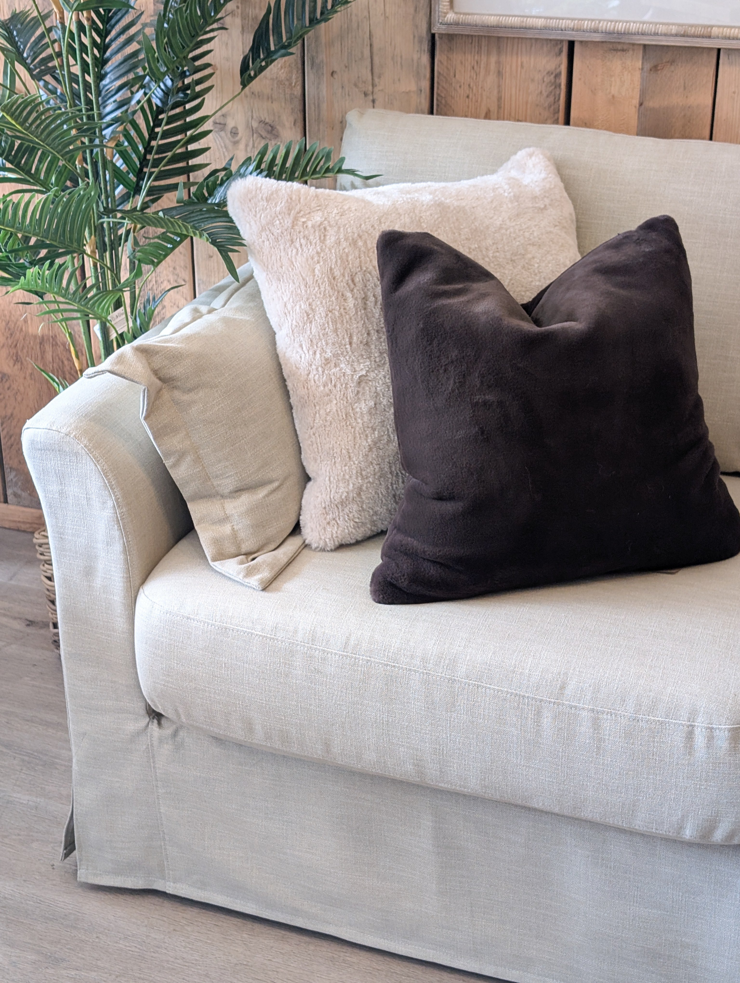 Beige sofa with decorative pillows against a wooden wall