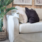 Beige sofa with decorative pillows against a wooden wall with framed artwork