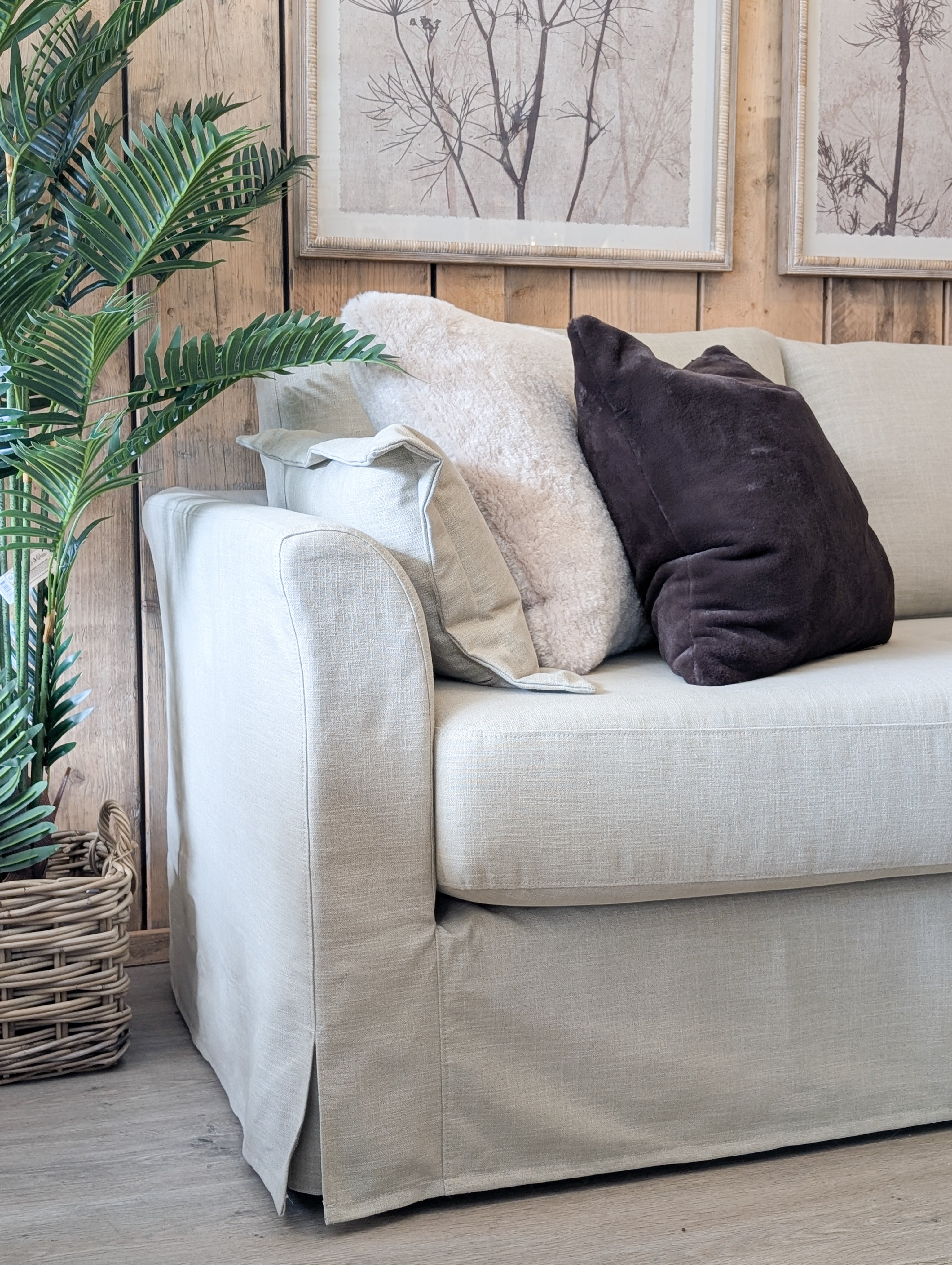 Beige sofa with decorative pillows against a wooden wall with framed artwork