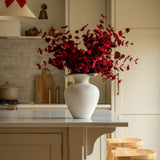 Kitchen with a white vase of red flowers on a counter, wooden stools, and a red bow decoration.