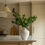 Kitchen with a white vase on a counter, plants, and wooden stools.