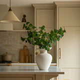 Kitchen with a white vase on a counter, plants, and wooden stools.