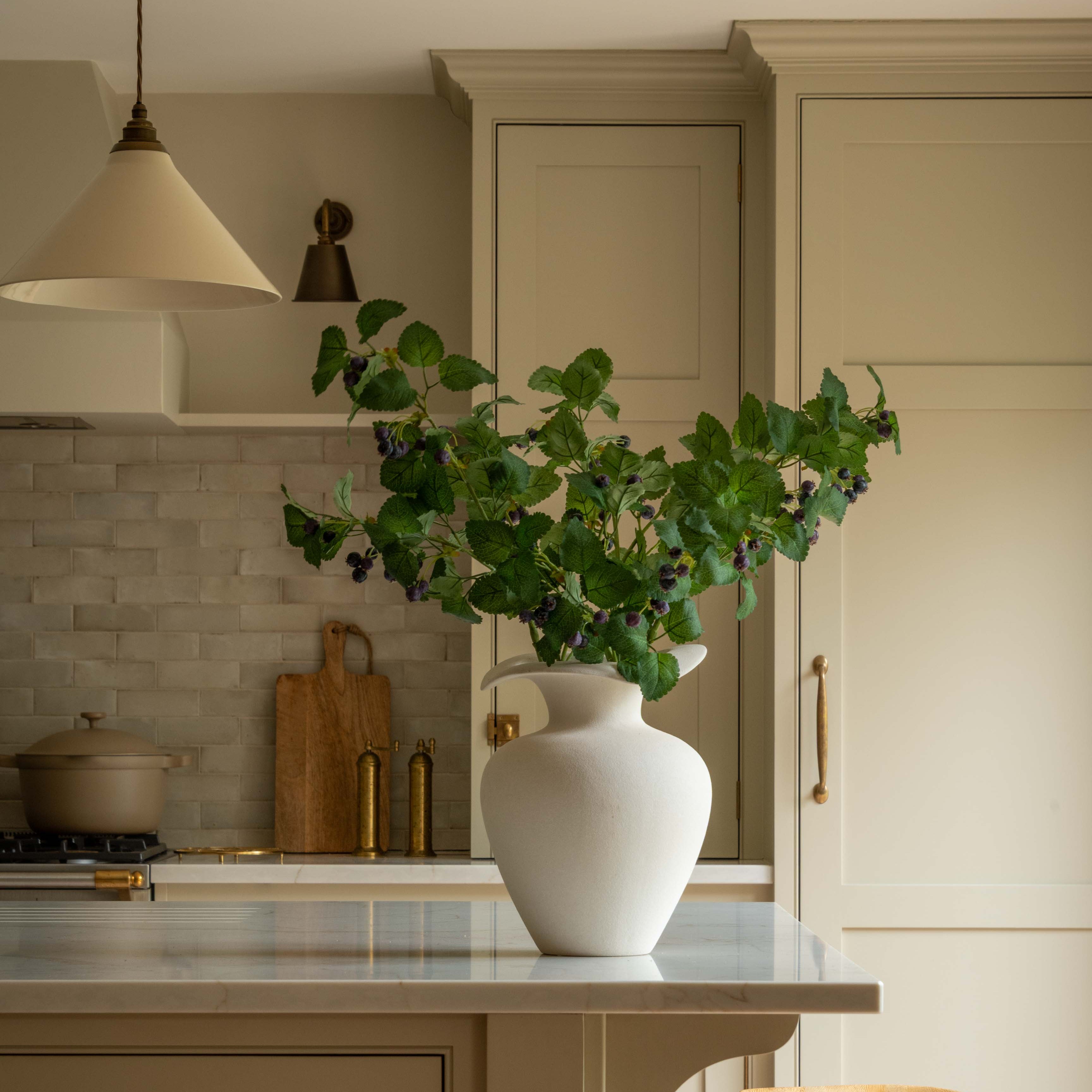 Kitchen with a white vase on a counter, plants, and wooden stools.
