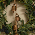 Decorative wreath with greenery and bronze bells on a neutral background